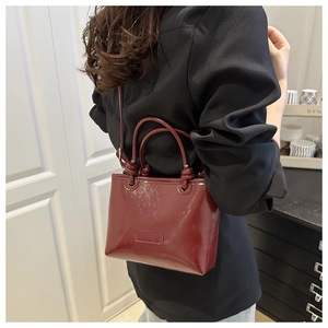 Detail view of burgundy patent leather tote bag with glossy finish and slim straps