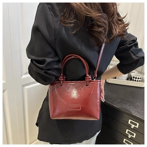 Detail of dark red glossy tote bag with knotted handle and sleek crossbody strap