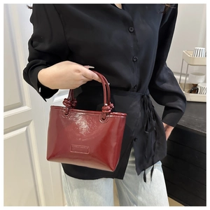 Detail of burgundy patent leather tote bag showing glossy texture and knot handle