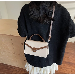 Détail d'un sac bandoulière bicolore beige et marron en daim avec une boucle métallique