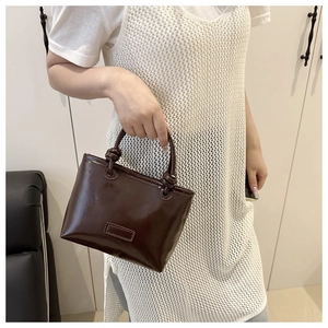 Detail of a dark brown glossy leather mini tote bag with unique knotted handle design