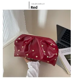 Détail de la pochette froncée rouge foncé avec clous dorés dans un décor de bureau moderne