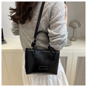 Detail view of the black patent leather tote bag with shiny finish and adjustable strap