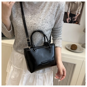 Chic black patent leather tote bag detail with knot handle design and crossbody strap