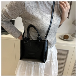 Detail of a black glossy patent leather crossbody bag shown on a model in a minimal setting