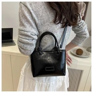 Detail view of glossy black faux leather crossbody tote bag worn by a fashion model