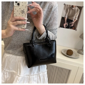 Detail of a black patent leather mini tote bag with knotted handles on a white cabinet