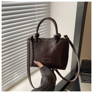 Detail of dark brown leather tote bag with knotted handles and adjustable strap
