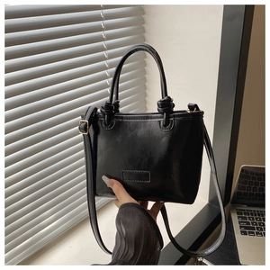 Detail of a black faux leather tote bag with round handles and adjustable shoulder strap