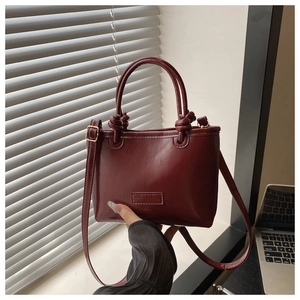 Detail of dark burgundy tote bag with knot handles and shiny patent leather texture