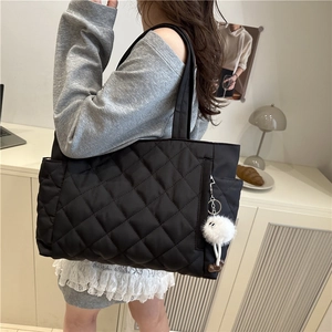 Black quilted tote bag with diamond pattern and plush charm on a female model