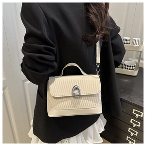 Close-up of beige woven shoulder bag with silver horseshoe buckle and leather strap