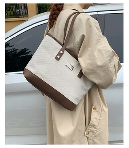 Detail of canvas tote bag with brown leather trim carried by a model in a trench coat