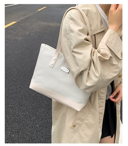 Outdoor shot of a white woven tote bag with leather handles and metallic logo plate