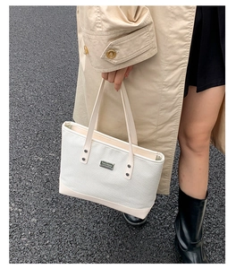 Dettaglio ravvicinato della borsa tote in tela bianca con finiture in pelle e logo