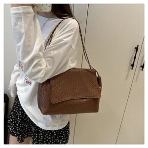 Détail d'un sac à bandoulière marron tressé avec une chaîne en métal élégante sur modèle