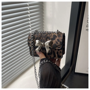 Close-up of leopard print mini bag with silver bow clasp and chain strap held by hand