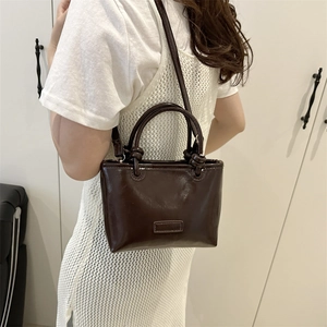 Dark brown glossy patent leather tote bag with top handles and adjustable shoulder strap