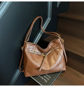 Detail view of large dark brown leather tote bag on wooden stairs with bronze hardware