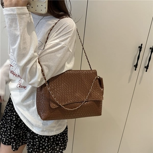 Sac à bandoulière tressé marron avec chaîne porté par un modèle, style vintage