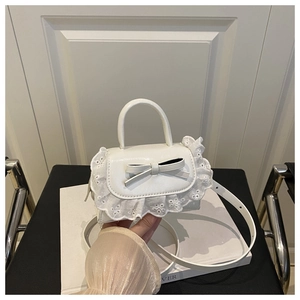 Detail view of white mini handbag featuring 3D leather bow and delicate lace trim edges