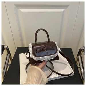 Detail of caramel brown mini handbag featuring lace trim and a central bow accent