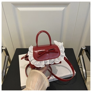 Close-up of red mini handbag with leather bow detail and white lace embroidery trim