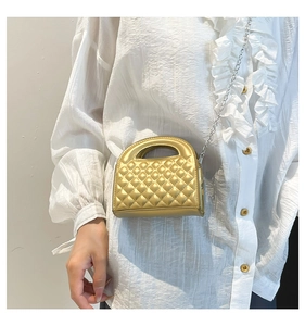 Close-up of golden quilted mini crossbody bag with silver chain strap on a white shirt
