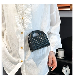 Detail of black quilted crossbody bag with silver chain strap worn by a model