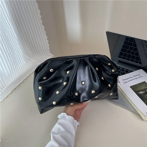 Pochette noire plissée avec clous dorés posée sur un bureau de style moderne
