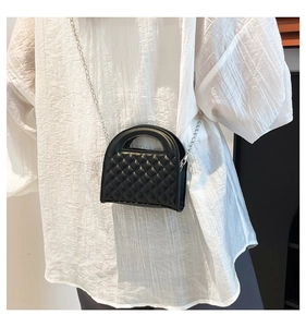 Detail of black quilted crossbody bag with silver chain strap and top handle on person