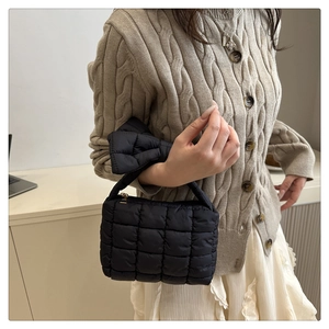 Detail of black quilted puff bag with bow handle and zipper, worn with a knit cardigan