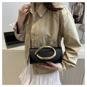 Detail of black faux leather crossbody bag with a large irregular gold metal buckle