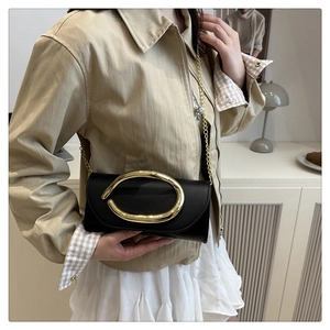 Detail of elegant black leather clutch with oversized golden ring buckle and chain strap
