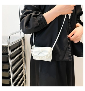 Detailed view of mini white bow crossbody bag with lace trim on a female model