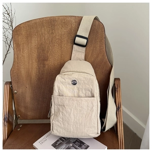 Detail showing high-quality beige nylon fabric texture and round metal logo on crossbody bag