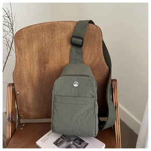 Detailed close-up of olive green nylon chest bag with a metallic M logo on a wooden chair