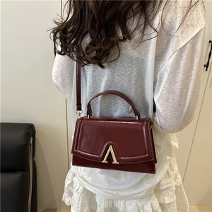 Burgundy oiled leather handbag with gold metal clasp shown on a model