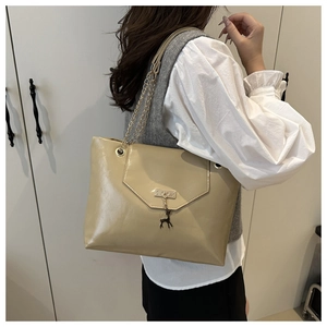 Detail of beige faux leather tote bag featuring a decorative metal elk charm and chain strap