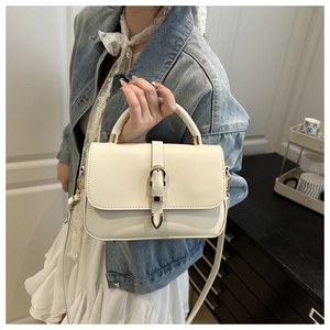 Close-up of cream leather crossbody bag with gold horseshoe buckle on model attire