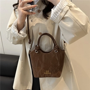 Brown pleated leather bucket bag with top handle and gold logo on beige trench coat