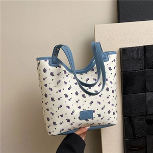 Floral tote bag with purple rose print and blue leather handles in a stylish hand-held pose