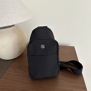 Minimalist black nylon crossbody sling bag for outdoors featuring a round metal logo