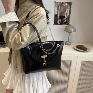 Fashionable black glossy tote bag with gold chain and deer charm in an elegant setting