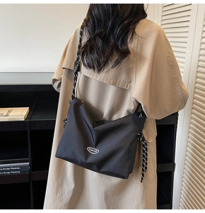 Detail of minimalist black crossbody bag with braided rope strap and oval logo on trench coat