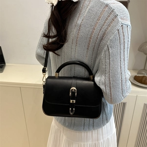 Classic black leather handbag with vintage gold buckle on light indoor background