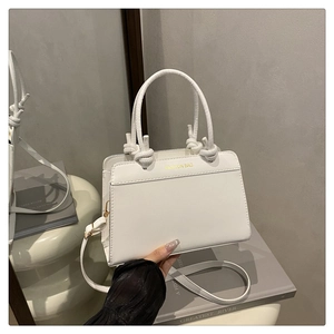 Close-up of white leather handbag with gold Fashion Bag text and knotted handle details