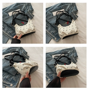 Dettagli di una borsa a mano bianca a pieghe con fiocchi neri e ciondolo a forma di ciliegia