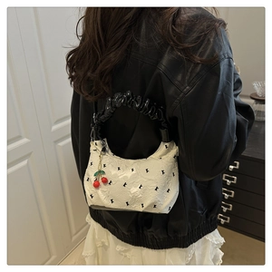 Detail of white dumpling bag with black K-letter embroidery and cherry charm pendant