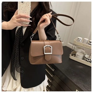 Detail of a brown leather crossbody bag featuring a large silver buckle and adjustable strap